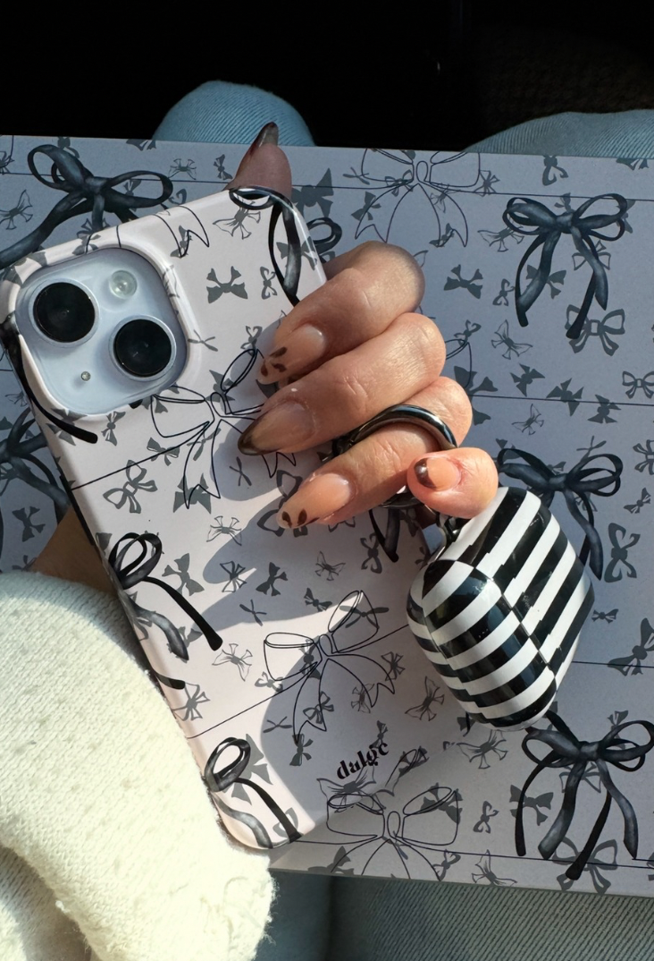 Icon featuring a hand holding a vibrant phone case adorned with bows alongside a striped AirPods case, set against a playful pink background decorated with bows."