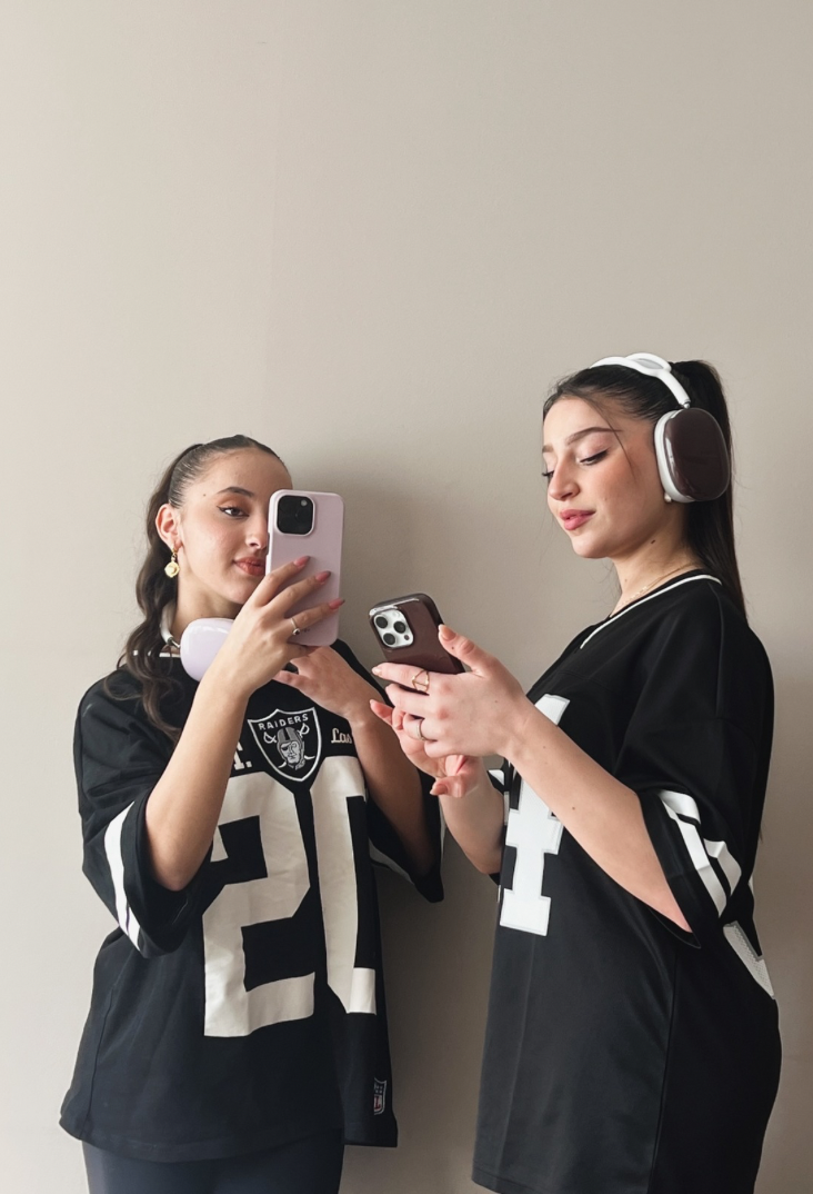 Icon featuring two girls dressed in sporty black and white clothing, each wearing AirPods Max and showcasing glossy designed cases, highlighting stylish audio accessories.