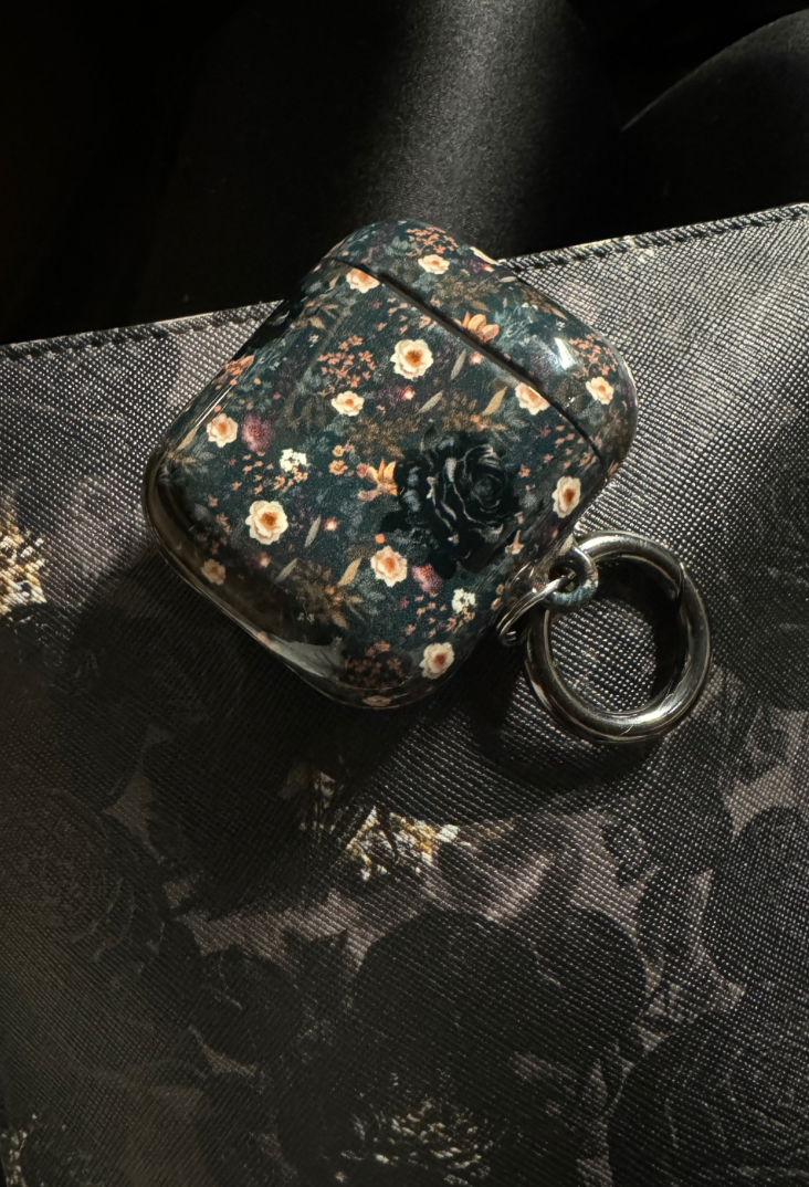 "A glossy designed AirPods case displayed on top of a dark floral bag, showcasing its stylish appearance."