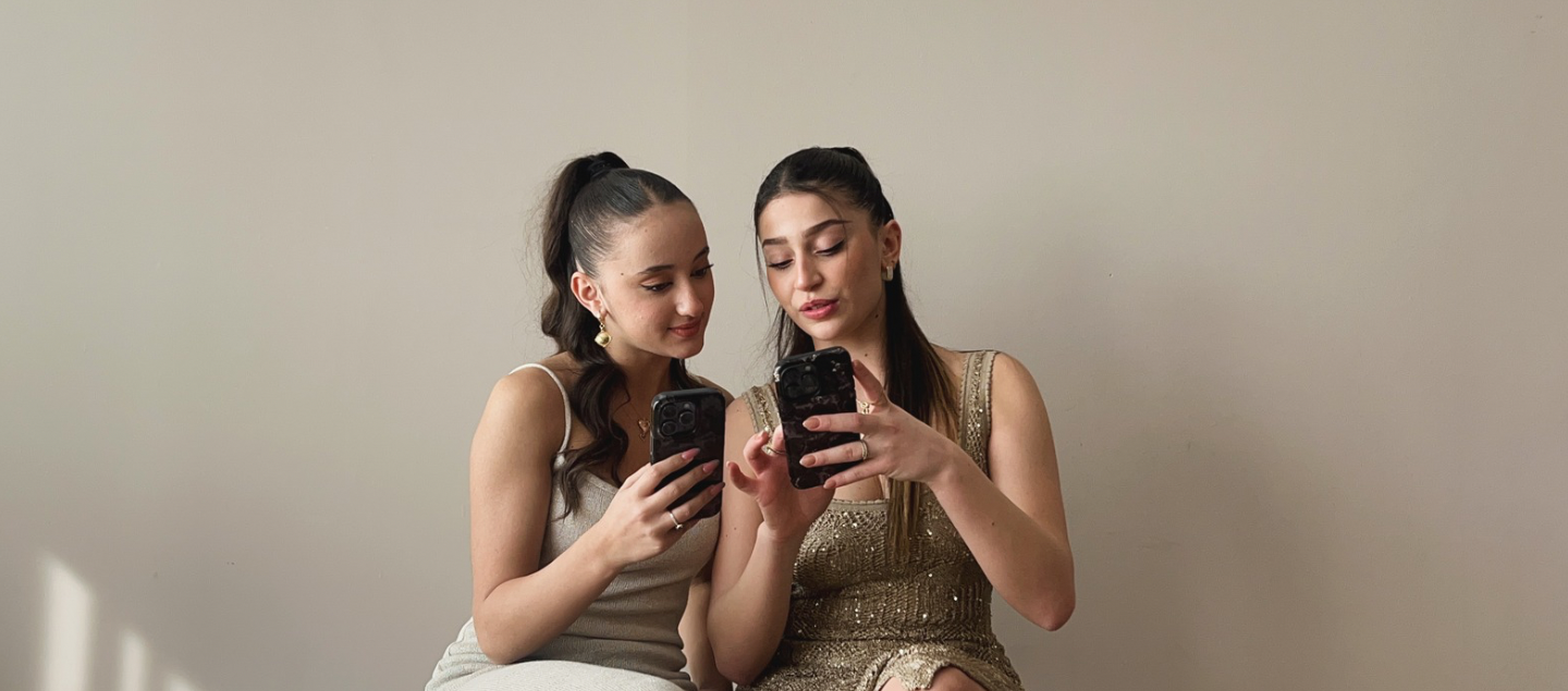 Main banner featuring two girls in beige dresses sitting together, smiling at each other while holding floral-designed phone cases against a natural beige wall." There are buttons with shop now for two different collections.